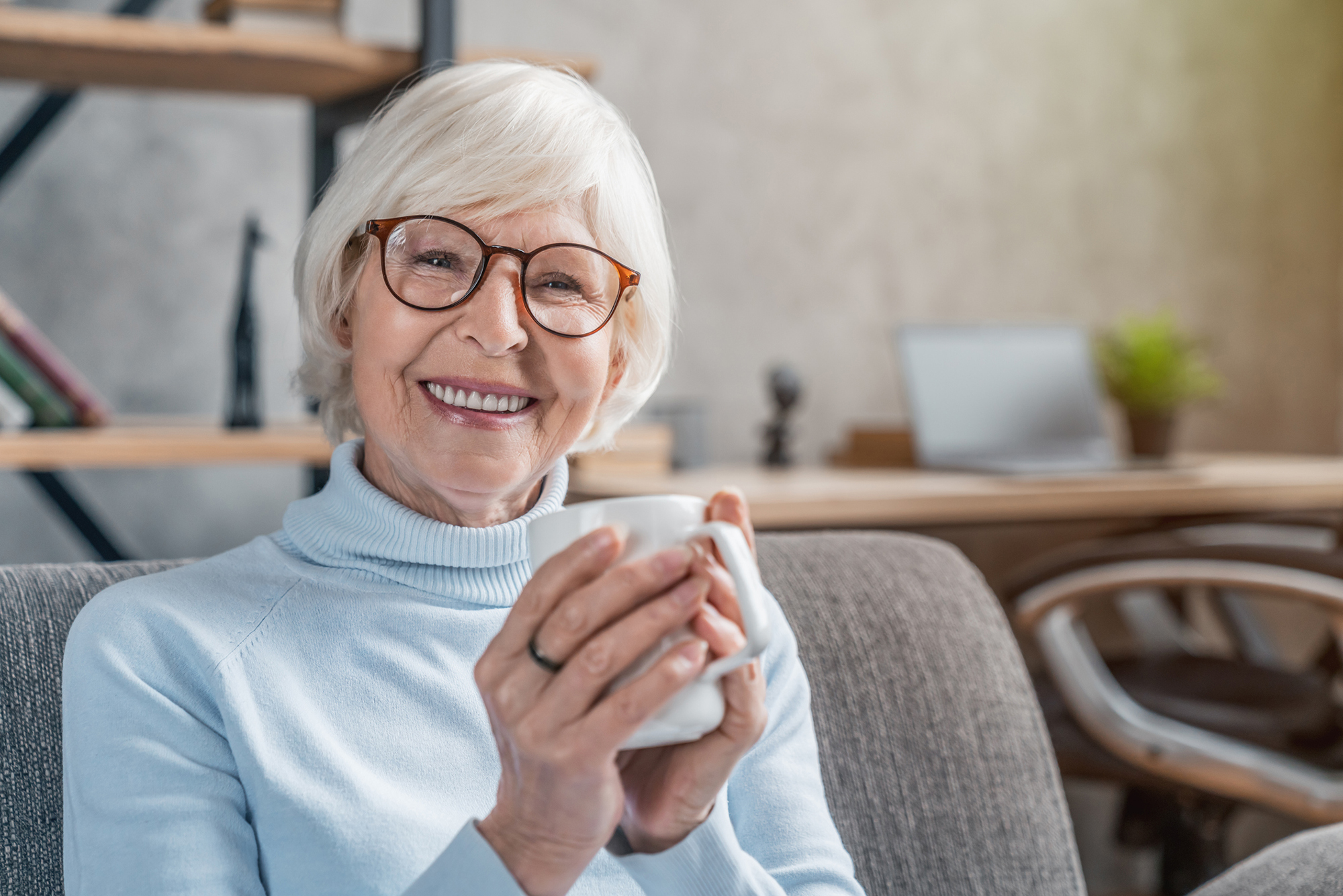 Senior woman drinking hot drink sitting on sofa at home