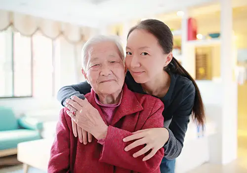 woman smiling as she hugs her senior mother
