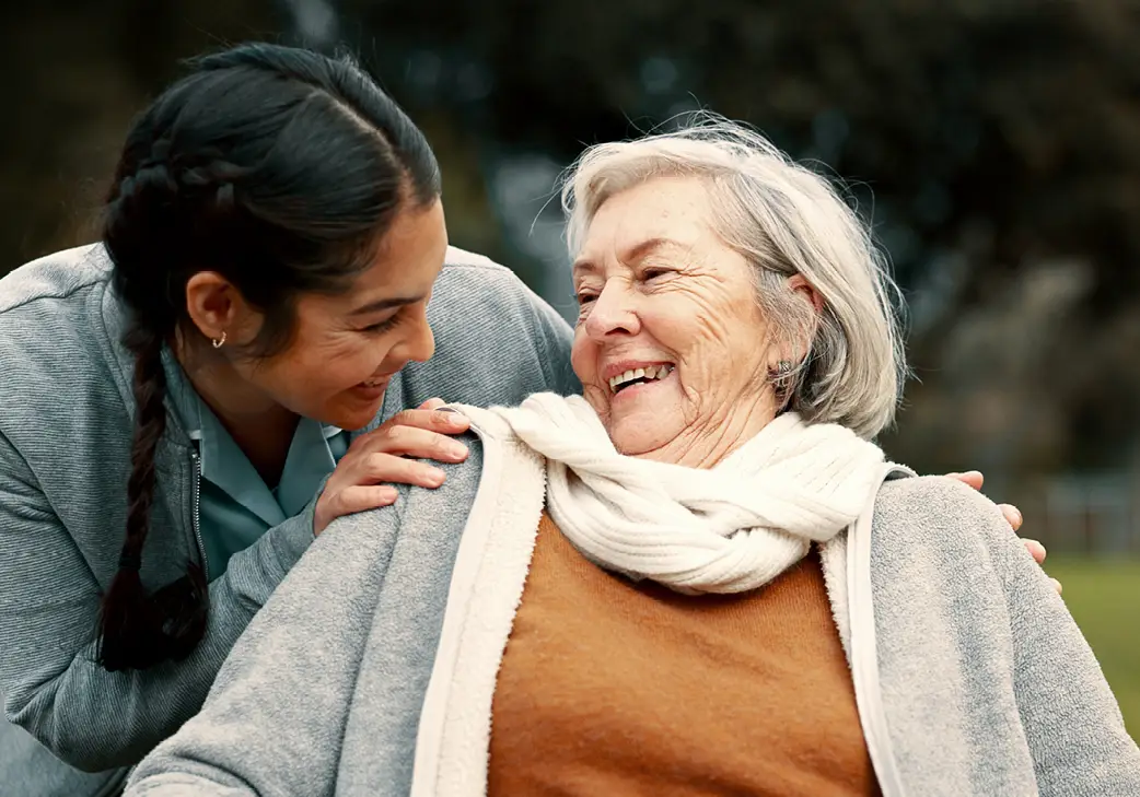 a senior woman and her granddaughter laughing together outside on a fall day